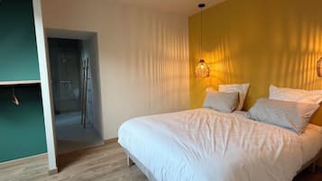 A bedroom with a bed, a hanging light fixture, and a wooden floor.