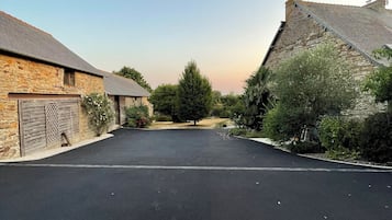A paved driveway leading to stone buildings with a clear sky above.