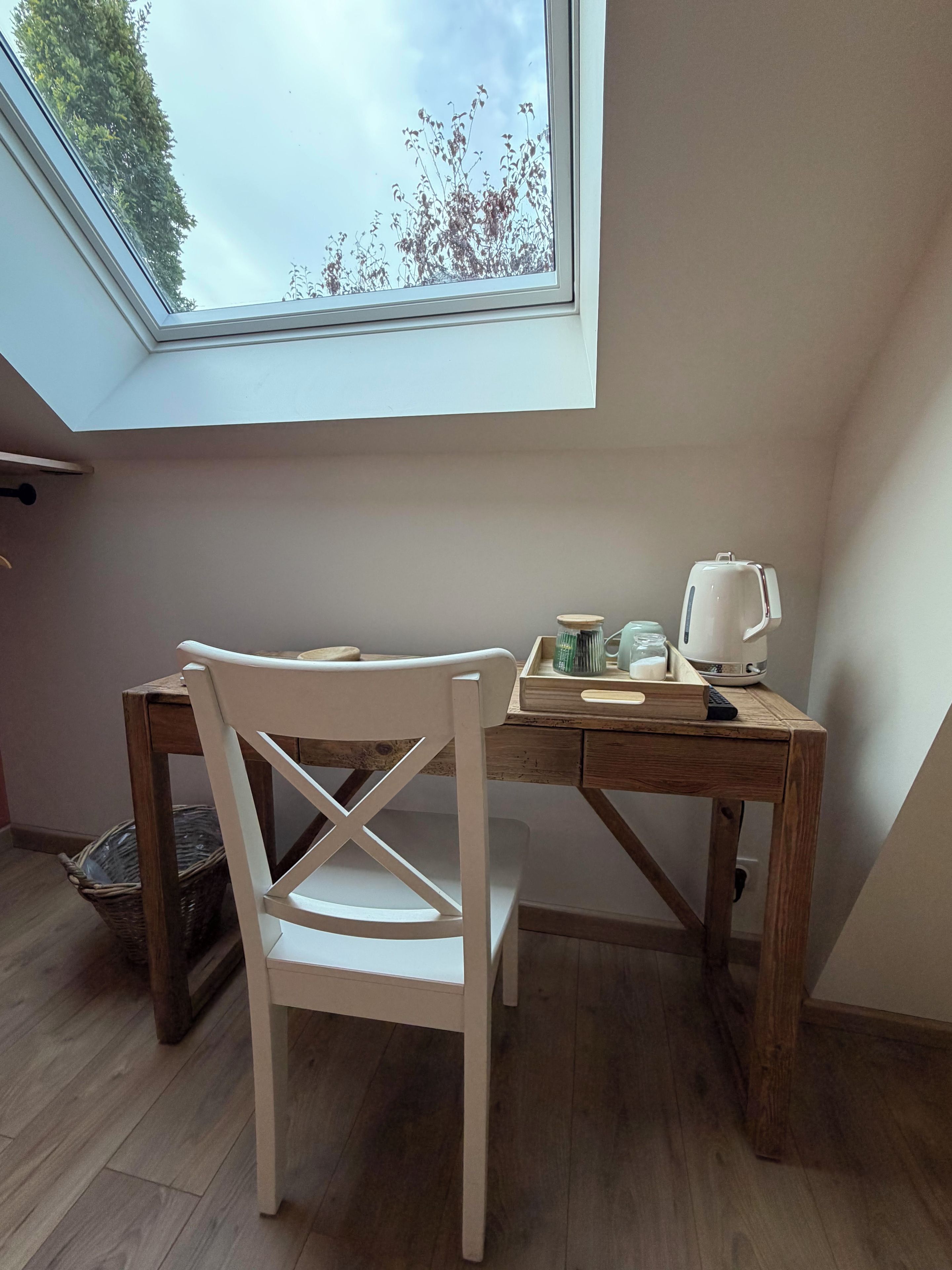 A room with a skylight, a wooden desk, a white chair, and a kettle.
