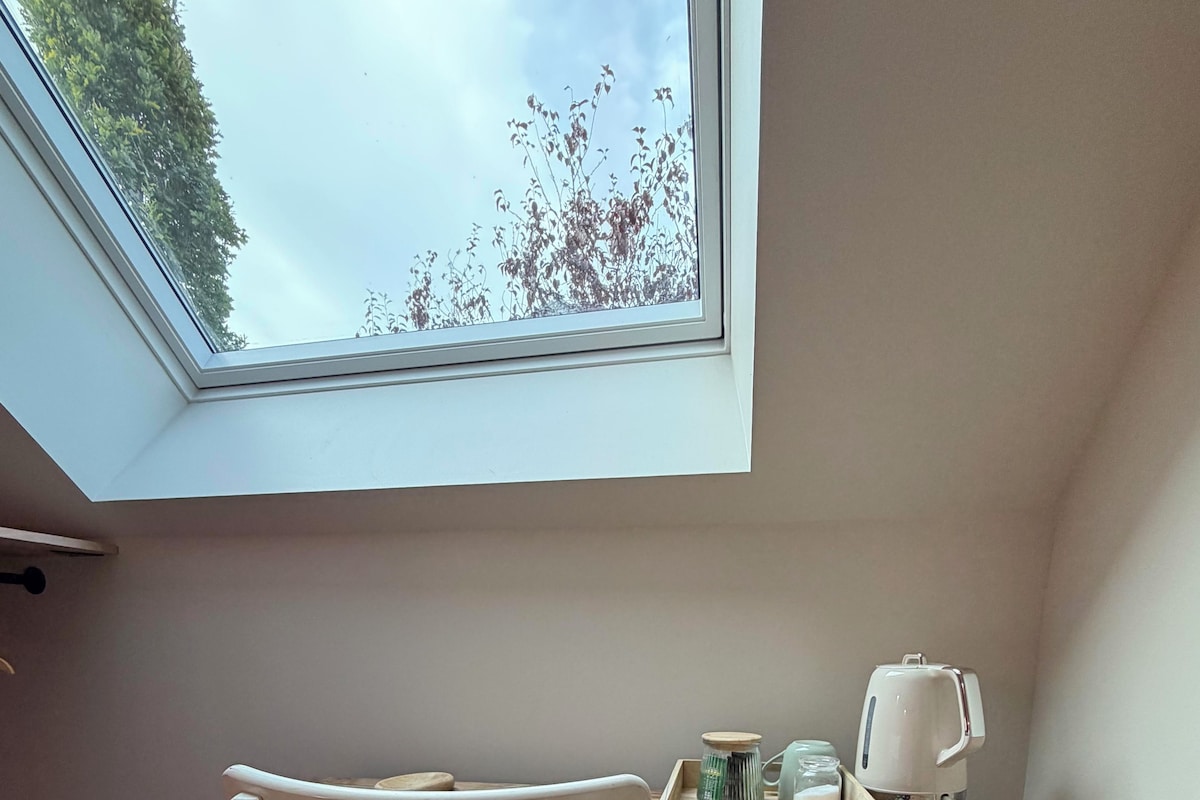 A room with a skylight, a wooden desk, a white chair, and a kettle.