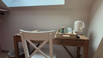 A room with a skylight, a wooden desk, a white chair, and a kettle.