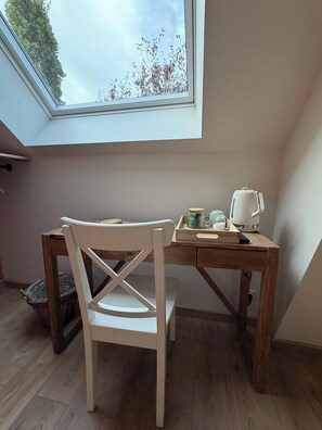 Ein Zimmer mit einer Dachfenster, einem Holztisch, einem weißen Stuhl und einem Wasserkocher.
