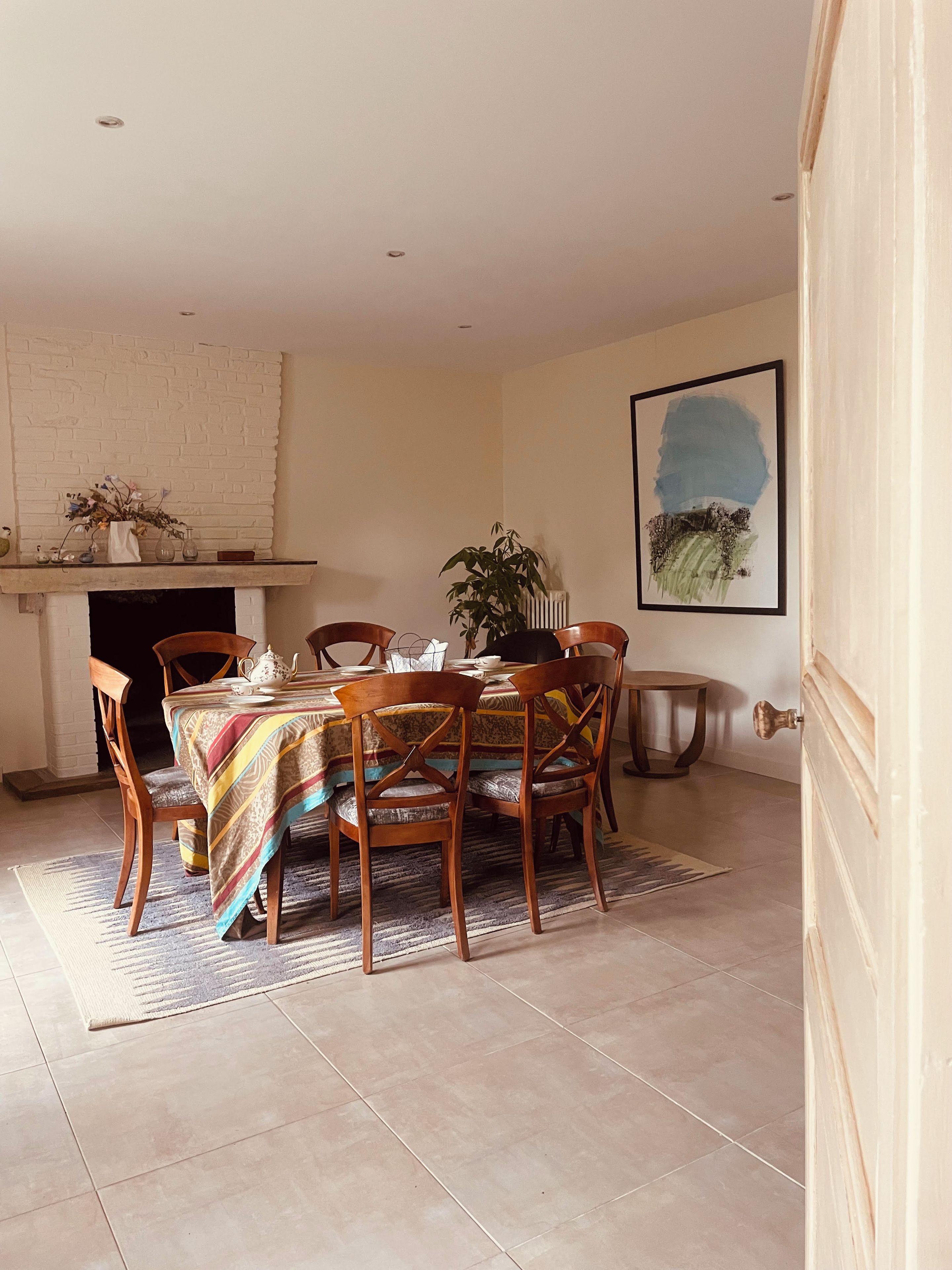 A dining area with a table set for four, surrounded by wooden chairs, a patterned rug, and a fireplace.