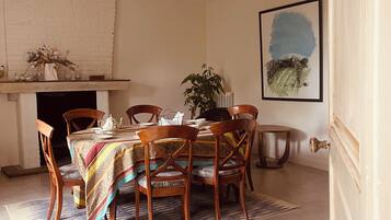 A dining area with a table set for four, surrounded by wooden chairs, a patterned rug, and a fireplace.