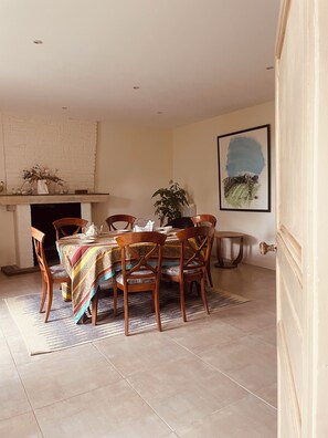 Un coin repas avec une table dressée pour quatre personnes, entourée de chaises en bois, d’un tapis à motifs et d’une cheminée.