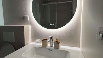 A bathroom with a round mirror, a white sink, and a shower visible in the background.