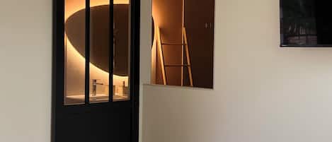 A bedroom with a bed, a black sliding door with a lit interior, a mounted air conditioner, and a framed picture on the wall.