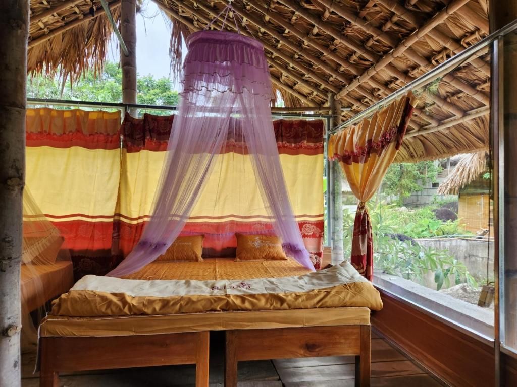 Ein Zimmer mit einem Bett unter einem Moskitonetz, Holzboden und Blick auf Grünfläche.