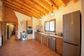 A kitchen with wooden beams, a stainless steel refrigerator, and a washing machine. - Masía among vineyards with pool in Catalonia (El Pla de Manlleu)