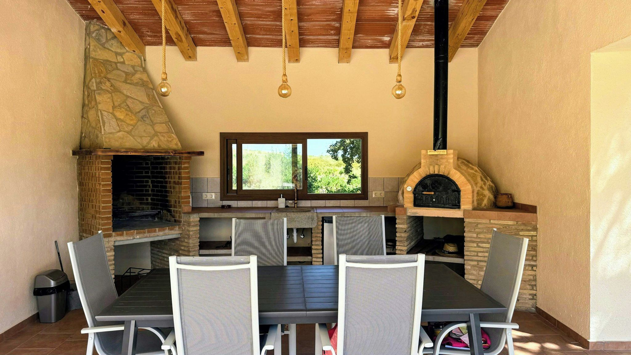 Un patio exterior con chimenea de piedra, horno de ladrillo y mesa con sillas.