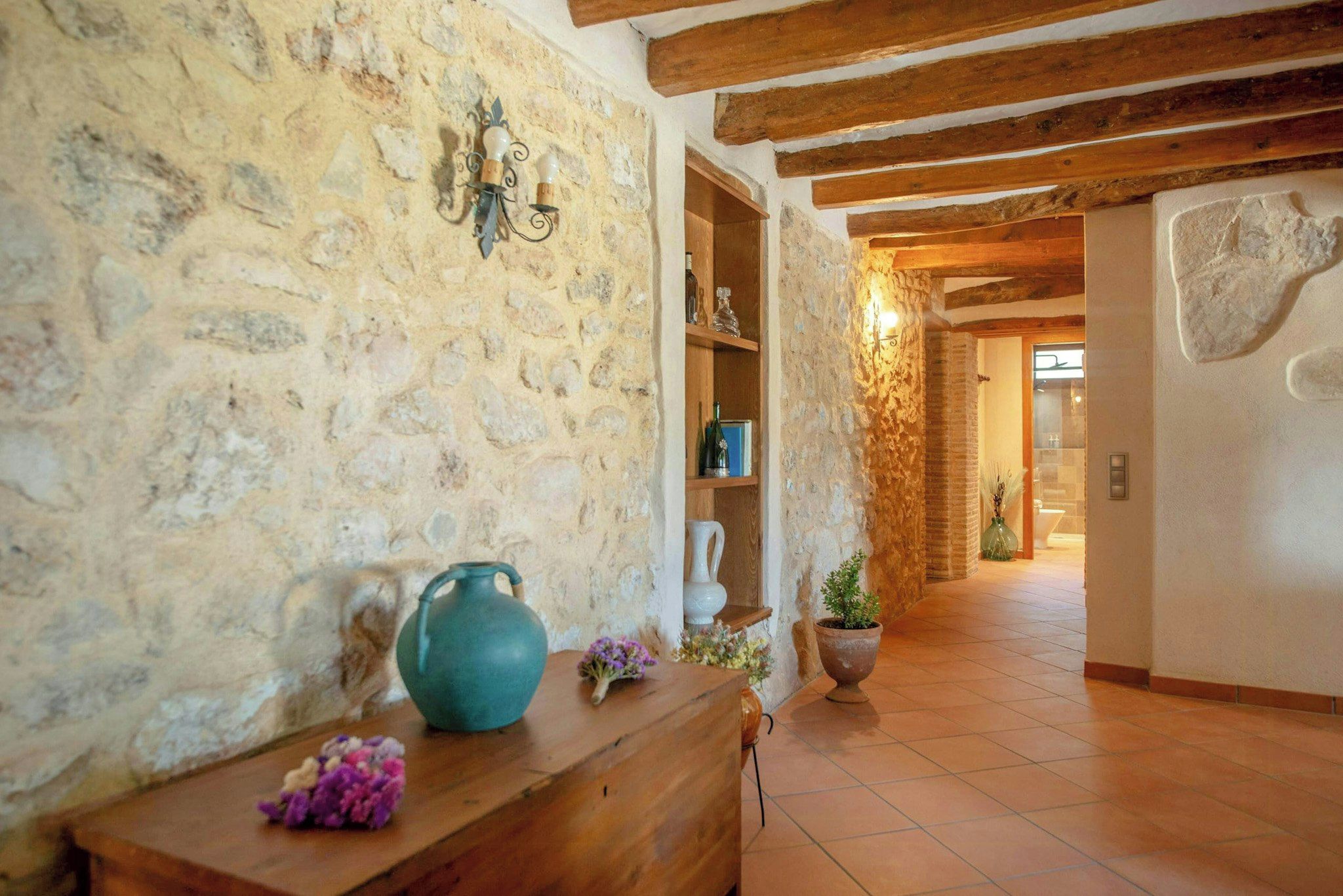 A stone wall with a rustic wooden bench, a ceramic jug, and a potted plant.
