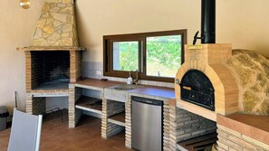 Una cocina con chimenea de piedra, ventana con vistas a la vegetación y un lavamanos de acero inoxidable.