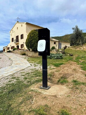 Un cuadro eléctrico exterior negro con un logotipo, situado en un césped con un camino de piedra que lleva a un edificio de techo de tejas.