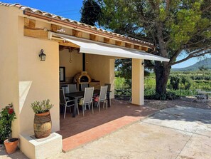 Une terrasse extérieure avec une table et des chaises, un four à pizza et des plantes en pot.