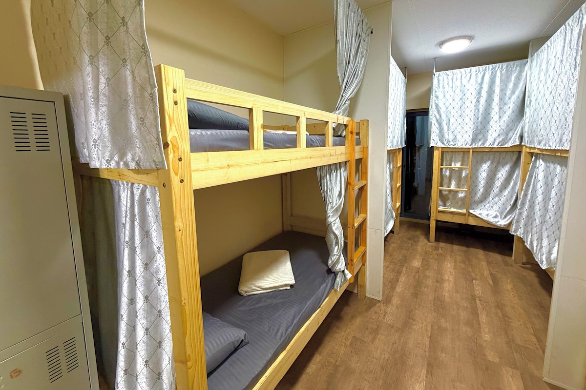 Une chambre avec un lit superposé en bois, un lit inférieur doté d’un matelas et d’oreillers, et une échelle.