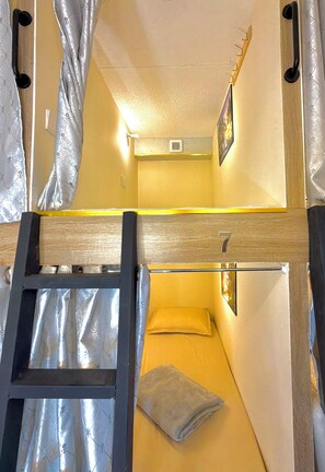 Un lit superposé avec une échelle, un lit simple, une petite fenêtre et un tableau accroché au mur.