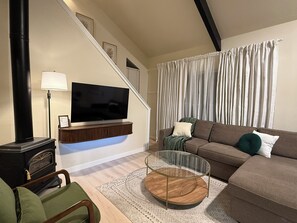 Ein modernes Wohnzimmer mit Flachbildfernseher, einer Couch, einem Glastisch und einem Kamin.