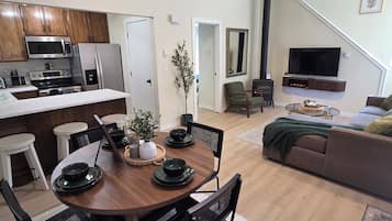 Cocina moderna con microondas, estufa y refrigerador. Hay un comedor con una mesa redonda y sillas, y una sala de estar con sofá y televisor.