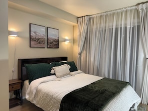 Ein Schlafzimmer mit einem Bett, zwei Wandleuchten, einem Nachttisch, einem dunklen Holz-Kopfteil und einem durchsichtigen Vorhang.