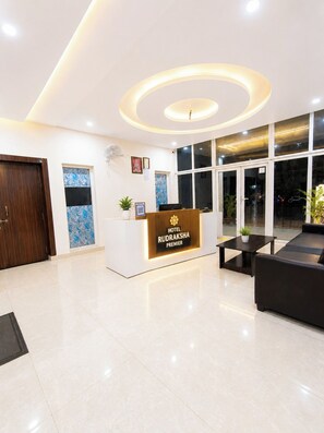 Zona de recepción de hotel con diseño moderno, que incluye un mostrador de recepción, un área de estar y ventanas amplias.