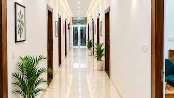 A hallway with a polished floor, framed artwork on the walls, and potted plants.