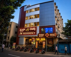 Un hotel con un letrero llamativo que dice 'JM Residency' y un restaurante cercano llamado 'Biryani Station'.