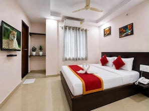 A hotel room with a bed, a ceiling fan, a window with curtains, a wall-mounted air conditioner, and a painting on the wall. - Hotel JM Residency (Bengaluru)
