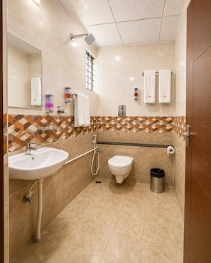 A bathroom with a sink, toilet, shower, and a patterned tile backsplash. - Hotel JM Residency (Bengaluru)