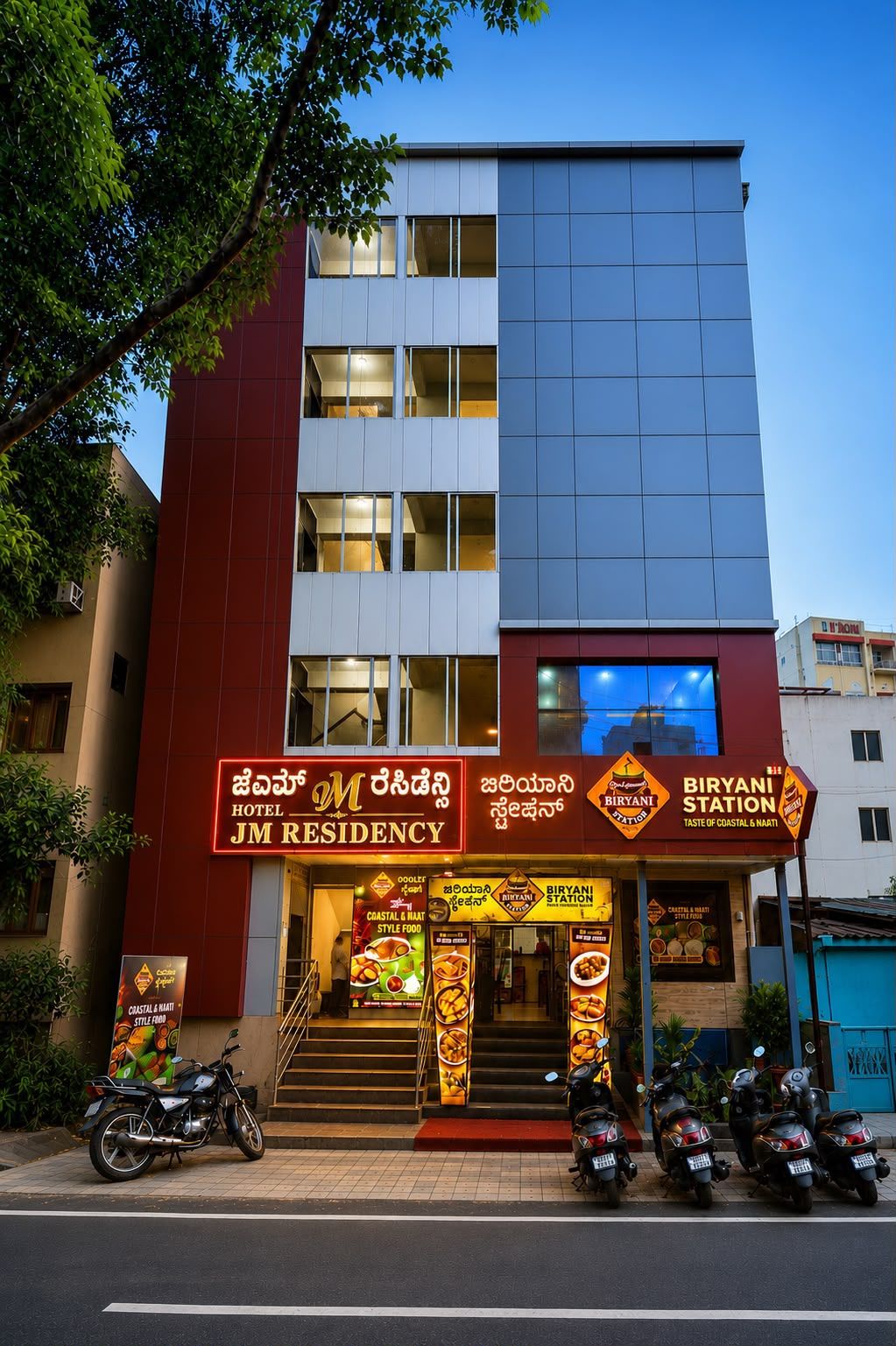 Un hotel con un cartel que anuncia 'JM Residency' y 'Biryani Station', publicando comida de estilo costero y naati.