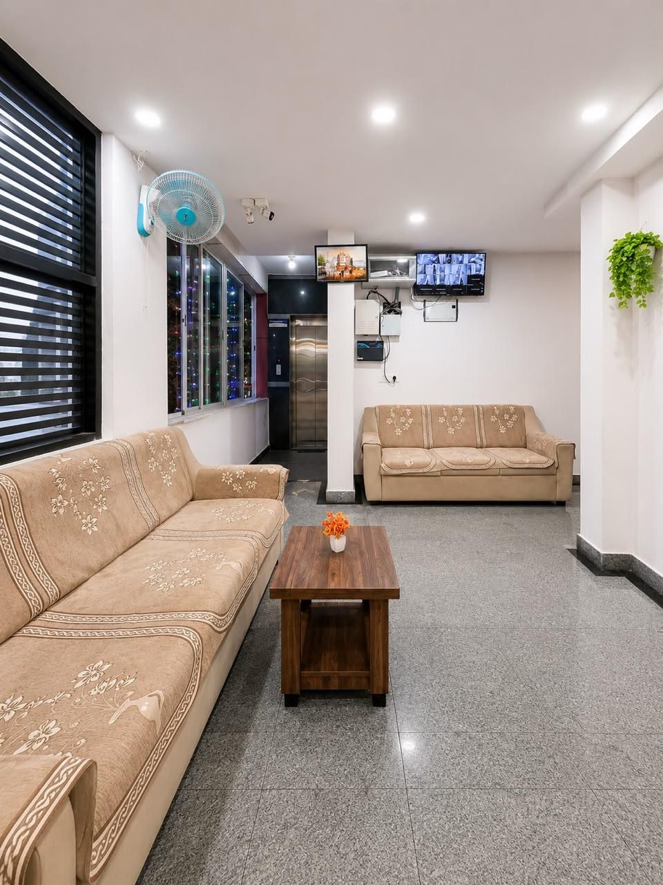 Eine Hotelhalle mit einer Couch, einem Couchtisch, einem Fernseher und einem Wandventilator.