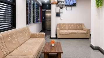 Eine Hotelhalle mit einer Couch, einem Couchtisch, einem Fernseher und einem Wandventilator.