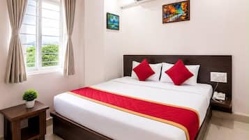 Ein Hotelzimmer mit Bett, Nachttisch, Deckenventilator, Klimaanlage, einem Fenster mit Vorhängen und einem Bild an der Wand.