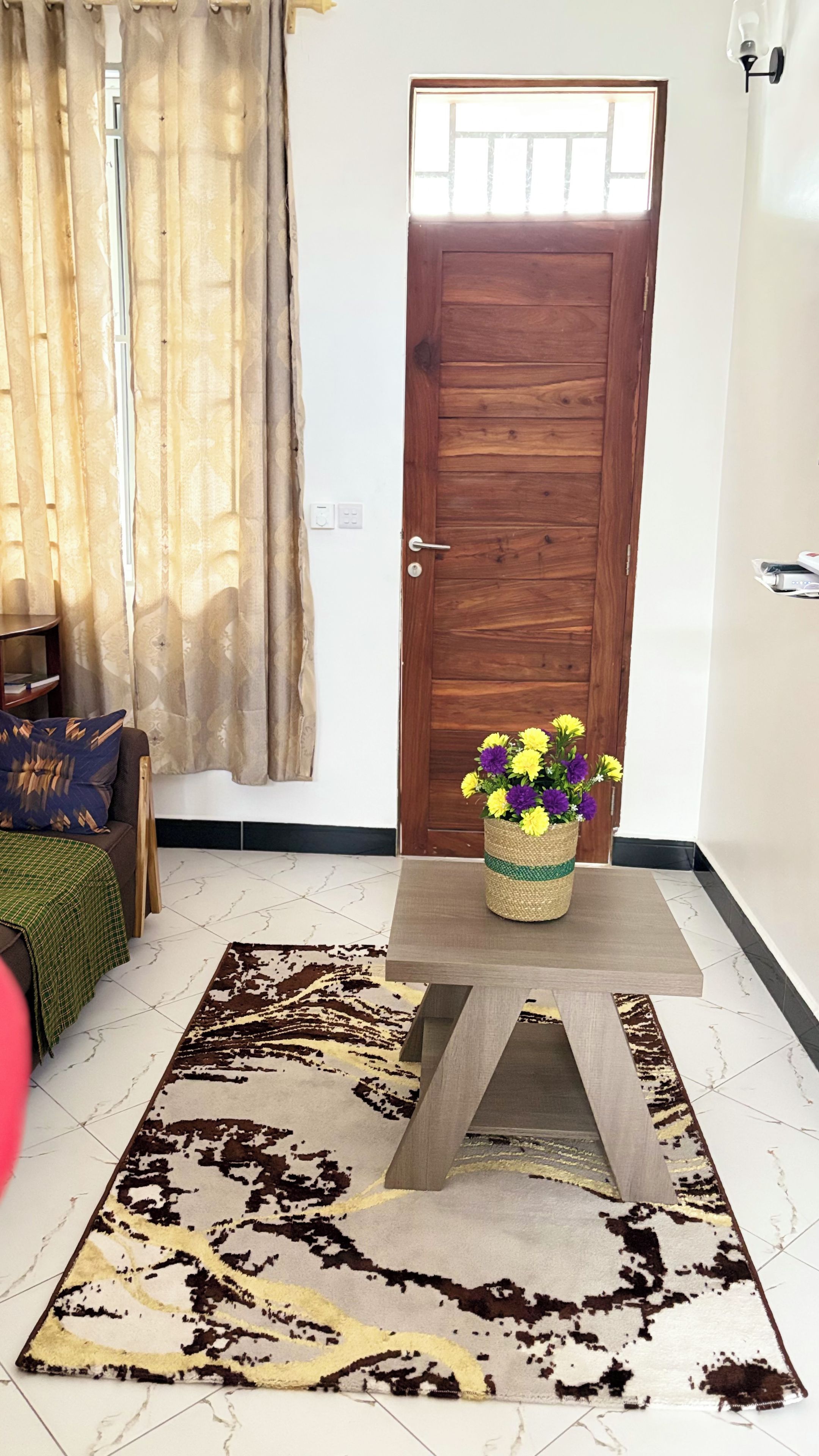 A room with a wooden door, a woven basket with flowers, a patterned rug, and a sofa with a green throw.