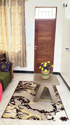 A room with a wooden door, a woven basket with flowers, a patterned rug, and a sofa with a green throw.