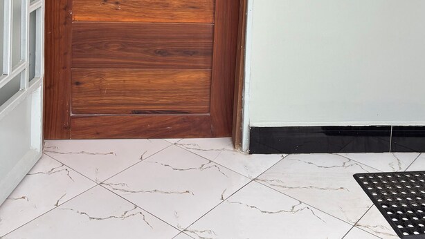 Una puerta de madera con manija metálica y cerradura, junto a una pared blanca y una ventana.