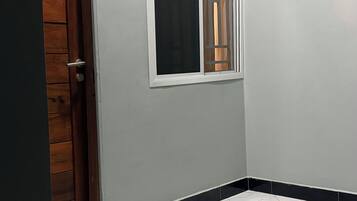 Um quarto com soalho em azulejo, porta de madeira e janela com moldura branca.