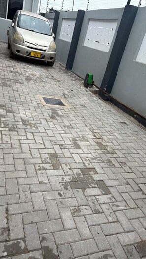 A paved driveway with a parked car and a wall with windows.