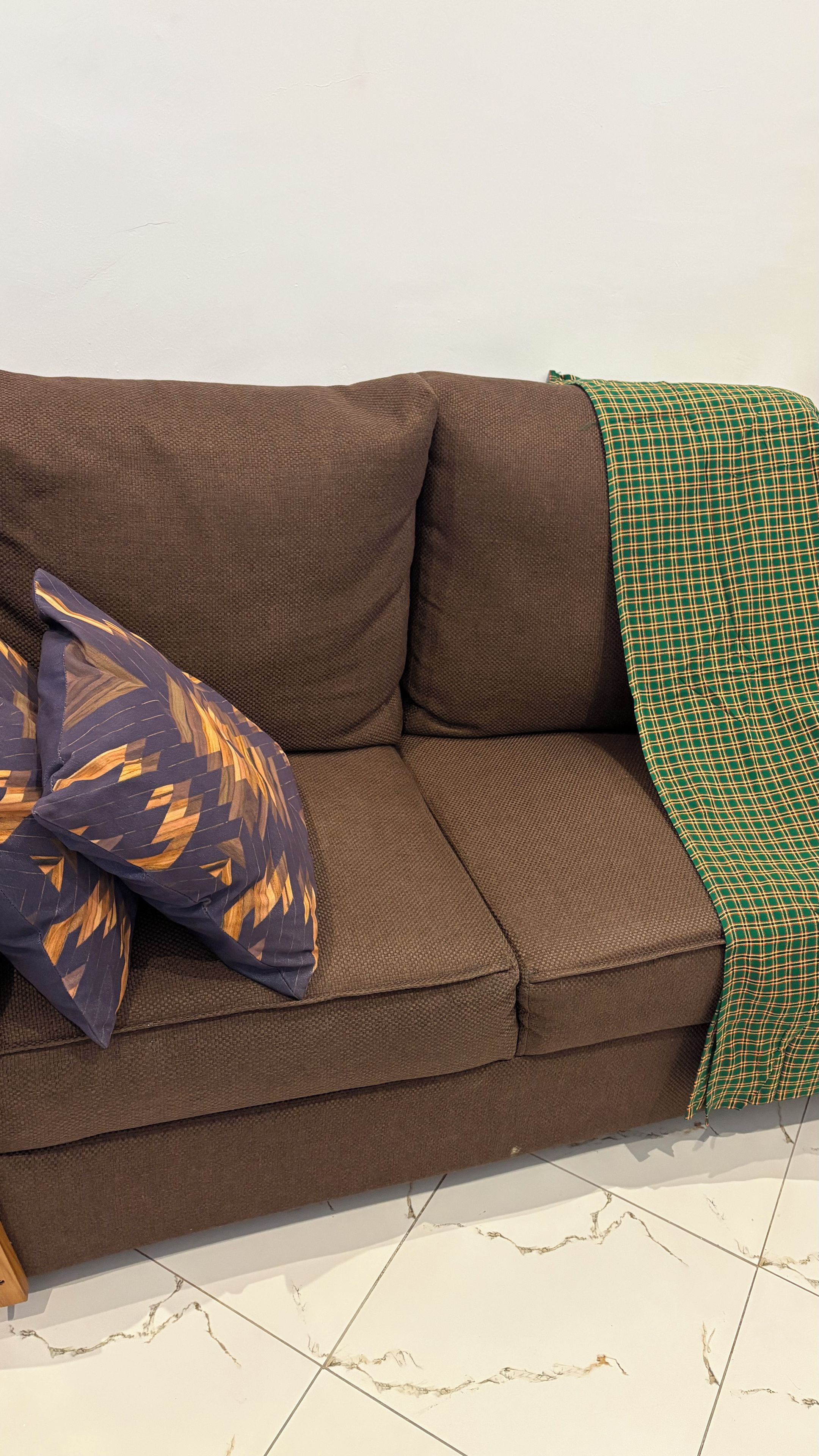 Un divano marrone con una coperta a quadri verdi e due cuscini decorati.
