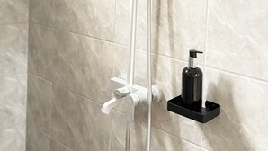 Ducha con cabezal de ducha manual y fijo, dispensador de jabón y un jabonera negra en la pared.