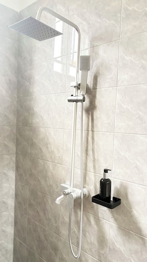 Eine Dusche mit Handbrause und fest installierter Duschköpfe, ein Seifenspender und eine schwarze Seifenschale an einer Wand.
