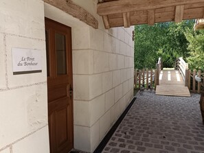 Ein Korridor mit einer Holztür, einem Schild mit der Aufschrift 'Le Pont du Bonheur' und einer Holzbrücke, die zu einer Grünanlage führt.