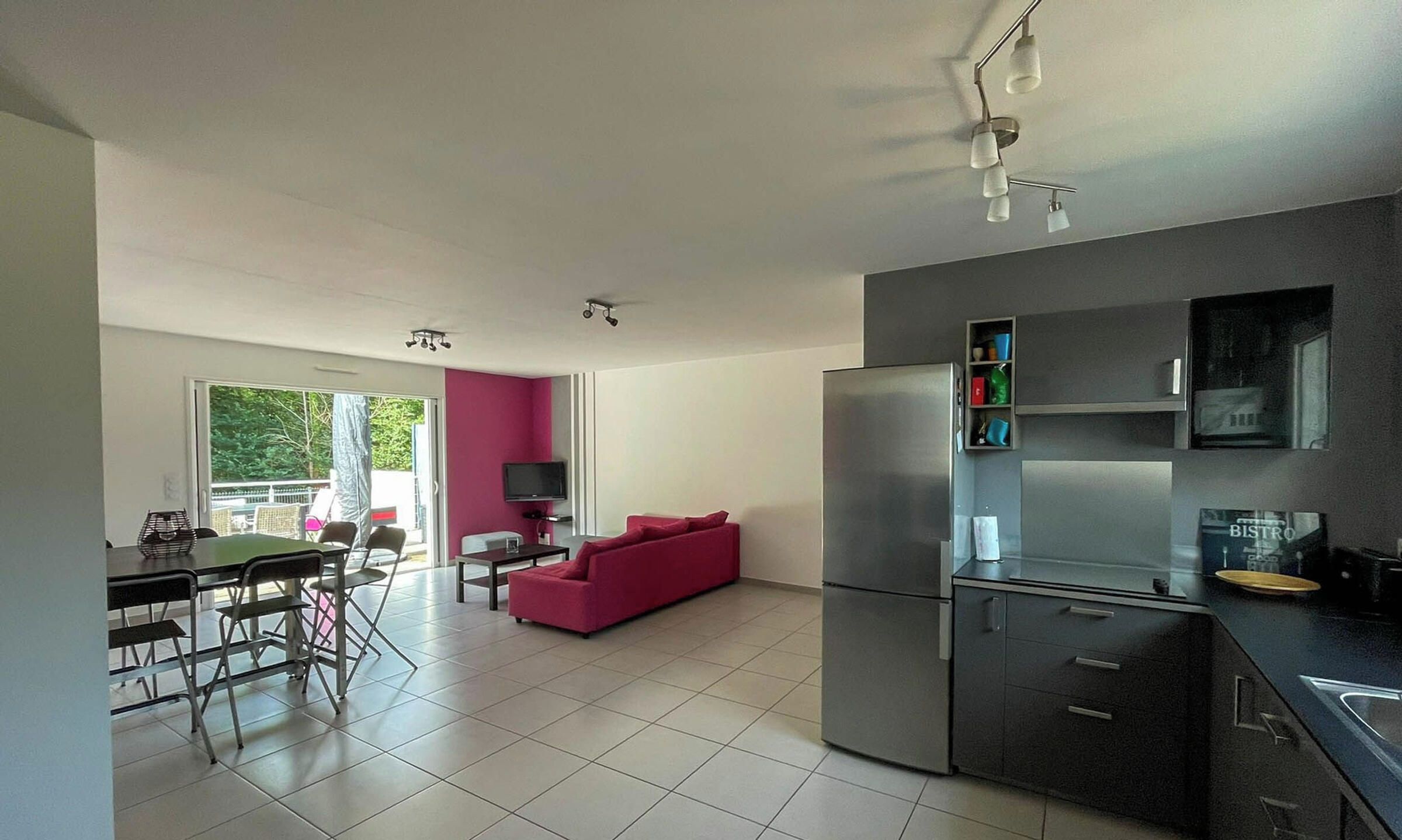 A modern kitchen with a refrigerator, a dining area with a table and chairs, and a living area with a sofa.