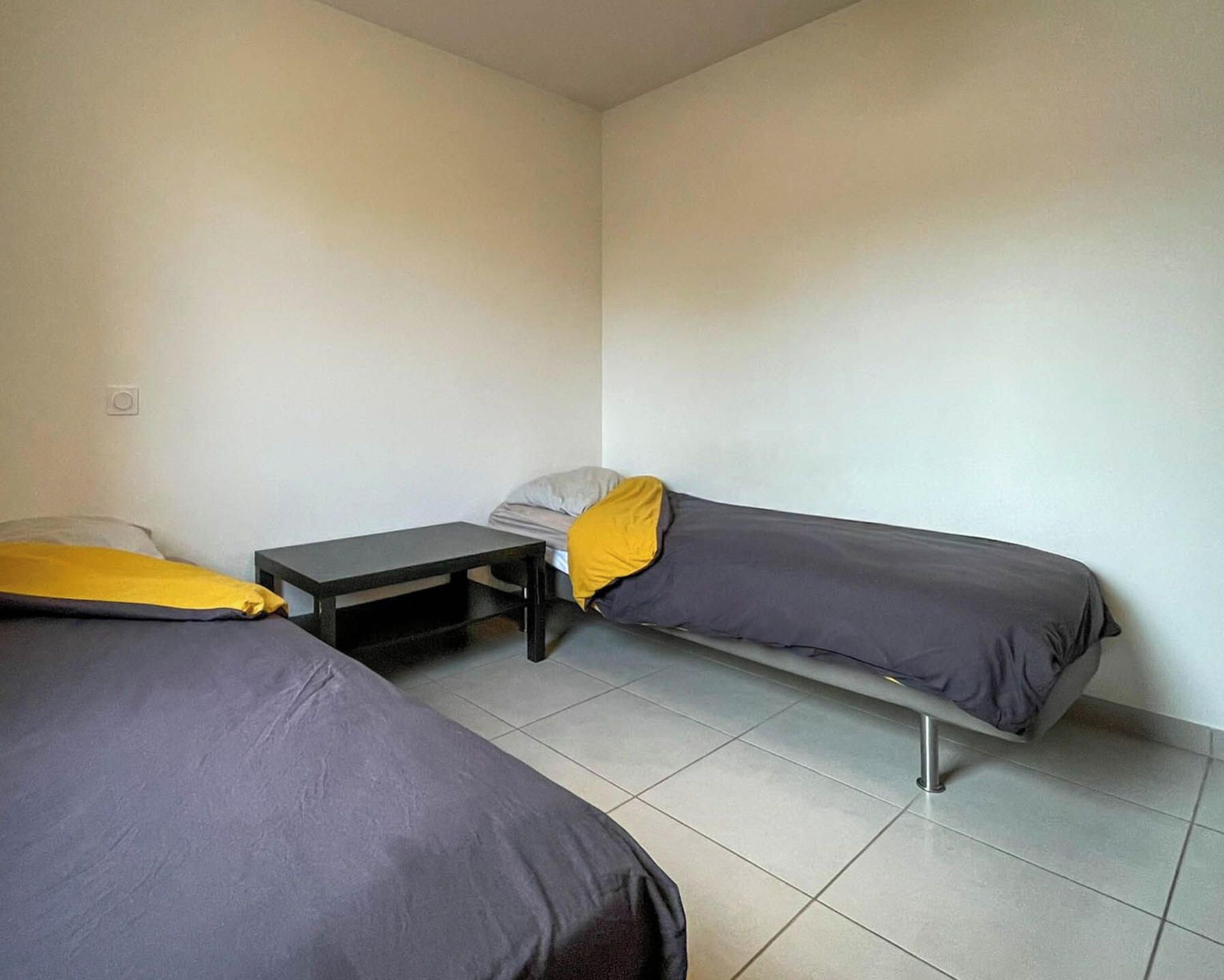 Una habitación pequeña y con pocos muebles, con dos camas individuales y una mesita.