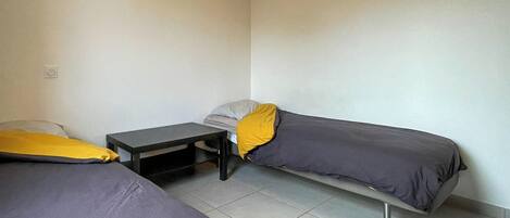 Una habitación pequeña y con pocos muebles, con dos camas individuales y una mesita.