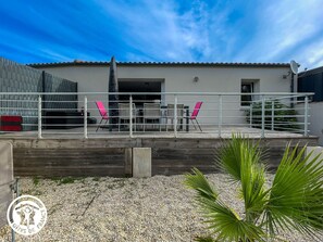 Un edificio moderno con techo plano, un patio cubierto con mobiliario exterior y suelo de grava.