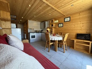 A cozy cabin interior with a dining area, kitchen, and a bed with red bedding. - Renovated mezzanine studio, terrace - 4/6 guests (Les Saisies)