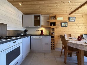 A compact kitchen with a stove, dishwasher, and wooden cabinets. - Renovated mezzanine studio, terrace - 4/6 guests (Les Saisies)