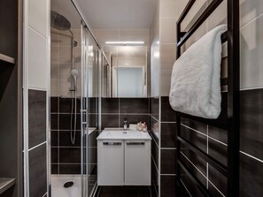 A narrow bathroom with a glass shower enclosure, a white sink with a mirror, and a towel hanging on a rack. - Renovated apartment with parking - 4 guests (Val-d'Isère)