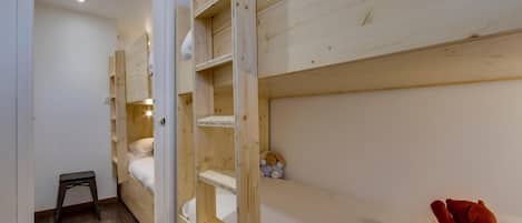 Ein Zimmer mit Etagenbetten, einem kleinen Hocker und einem Teddy auf dem Bett.