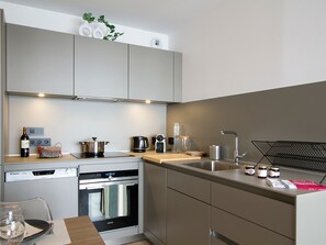 Eine moderne Küche mit integrierten Geräten, einem Essbereich mit Tisch und Stühlen sowie einer kleinen Pflanze auf der Arbeitsfläche.